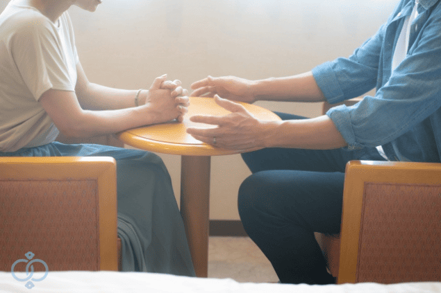 テーブルを挟んで向き合う男女の画像。彼の言い訳に対して、女性が冷静に話を聞きながら自分の答えを見出そうとしている場面を表現。