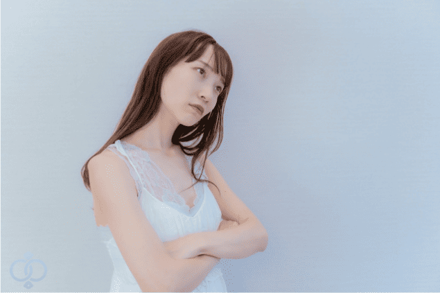 腕を組んで斜め上を見つめる女性の画像。交際中の相手が既婚者であると発覚した場合の責任について考えている場面を表現。