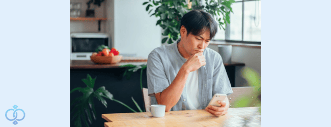 スマホを見ながら昔の友人の連絡先を探して悩む男性