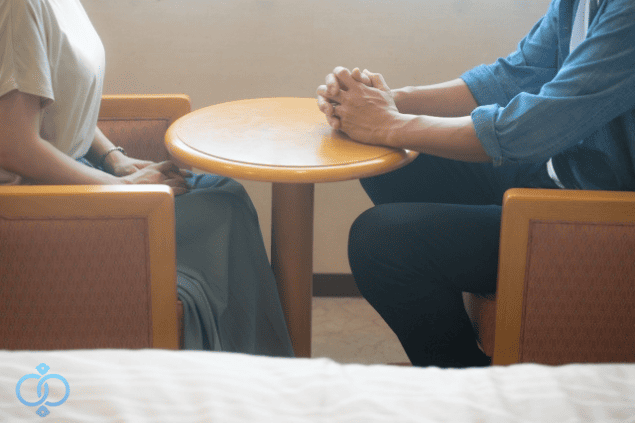 テーブルを挟んで向かい合う二人の画像。親子の会話や話し合いを通じて予防や解決策を見つける様子をイメージ。