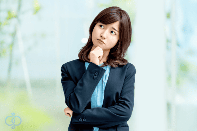 スーツ姿の女性が腕を組み、顎に手を当てて考えている画像。GPSを勝手に取り付けられた状況に対し、違法かどうか迷う読者心理を表現。