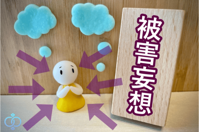 不安そうな表情の人形の周囲に矢印が向けられ、被害妄想と書かれた木の板