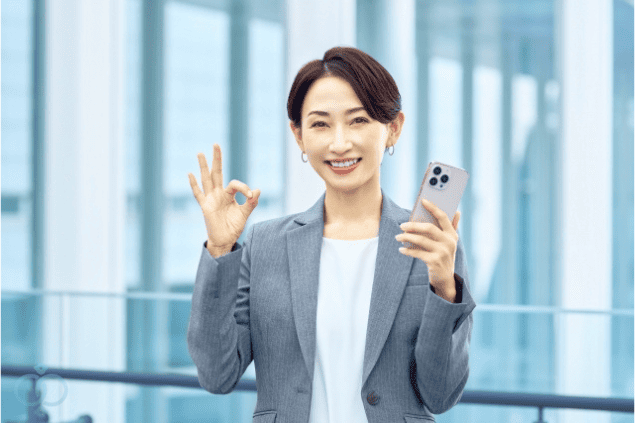 婚前調査(結婚前の浮気調査)で不安を解消し成功事例となった女性を象徴するイメージ画像。スマートフォンを持ちOKサインをする笑顔の女性が描かれ、依頼によって問題が解決し安心できたことを表現している。