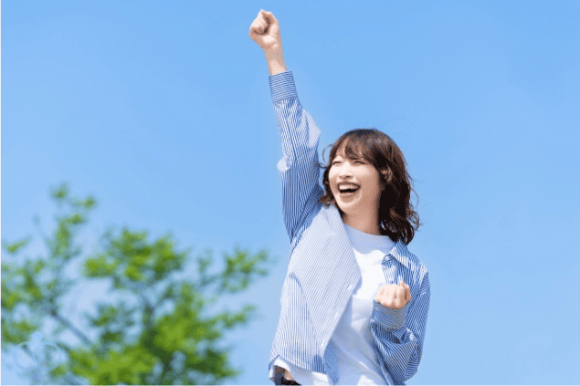 青空の下で笑顔でガッツポーズをする女性。ストーカー被害の不安を乗り越え、前向きな気持ちを取り戻したことを象徴する画像。