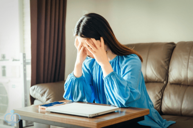 顔を手で覆い、スマホを前に悩み込む女性。既婚者の恋人との関係に苦しんでいる様子。