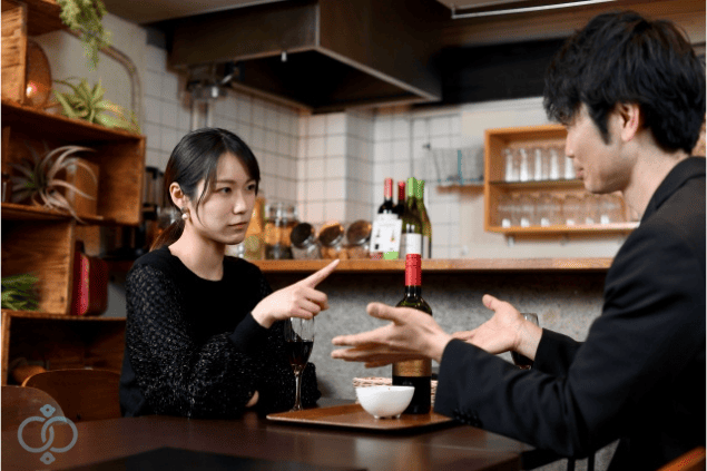 テーブル越しに彼氏を指差し、真剣な表情で問い詰める女性の写真。彼氏が既婚者だったと判明した後の対応を表す場面。