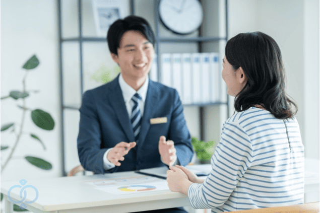 スーツ姿の男性と向き合って相談する女性。費用の不安をなくすために信頼できる探偵に正直に話している様子。