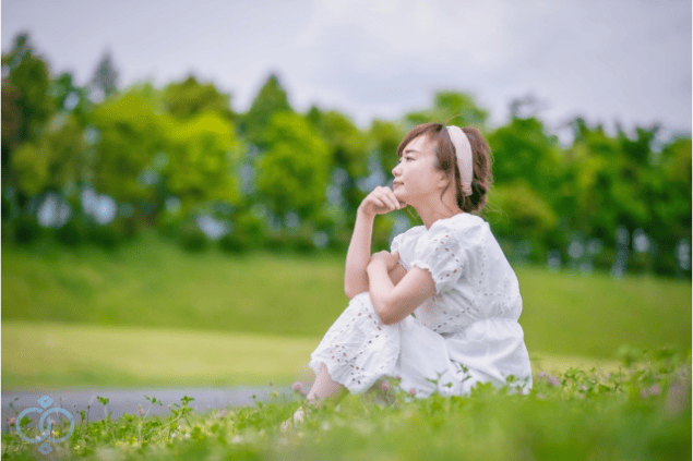 草原で遠くを見つめる女性。知らないままで終わらせず、真実と向き合おうとする静かな決意と勇気を表現。