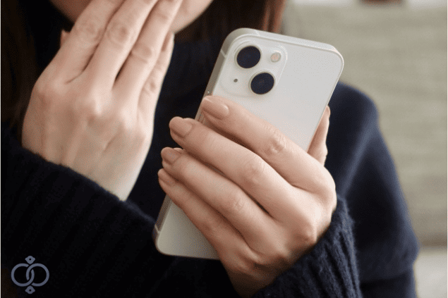 スマホを見ながら口元を押さえる女性の手元。身辺調査で彼が既婚者で子供までいたと知り、言葉を失った瞬間を表現。