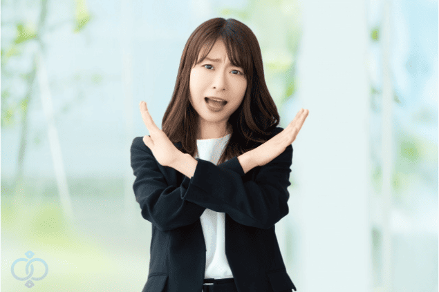 両手でバツ印を作っているスーツ姿の女性の画像。彼氏が既婚者かどうか調べる際に注意すべきNG行動を警告している様子を表現している。