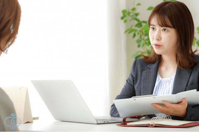 相談者に調査内容を説明しているスーツ姿の女性スタッフの画像。探偵への依頼を検討する際の相談シーンをイメージしている。