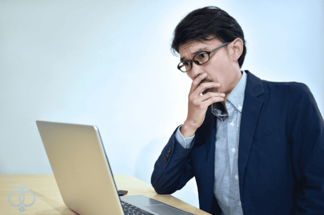 パソコンを見つめながら口元に手を当てて困惑している男性の画像。風俗嬢を自分で探す際の注意点や失敗リスクを表現。