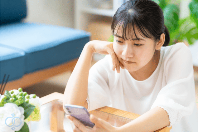 スマホを見つめて考え込む女性の画像。恋人が既婚者だと知りながらも別れられない理由に悩む様子を表現。