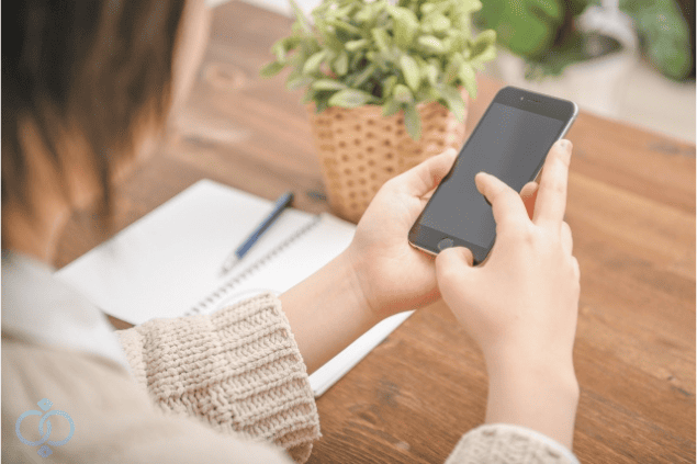 スマホを操作しながらノートとペンで情報を整理する女性の手元。旦那の素行調査を依頼する前に準備しておくことを示すイメージ画像。