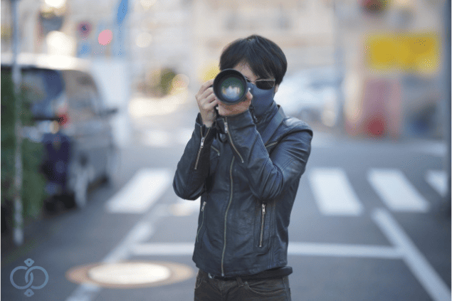 屋外で望遠カメラを構えて張り込み調査をする探偵の画像。風俗嬢の居場所を突き止めてお金を回収した流れを表現。