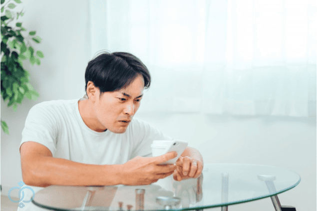 スマホを見て妻の様子に疑念を抱く男性の表情。妻の素行調査でおかしい理由を確かめるイメージ。