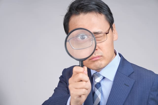 スーツ姿の男性が虫眼鏡で覗き込み、調査や確認をイメージさせる写真。結婚前調査のイメージ画像。