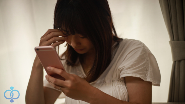 携帯をいじりながら頭を抱える女性