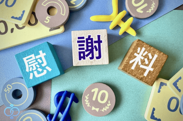 慰謝料と書かれたブロックの周りにお金のおもちゃが並んでいる様子