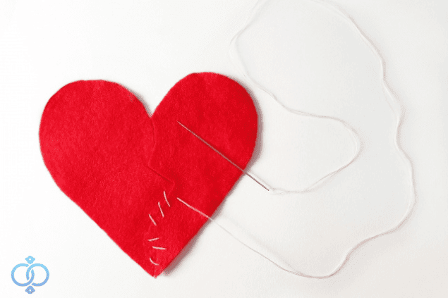 裂けた赤いハートを針と糸で修復している写真