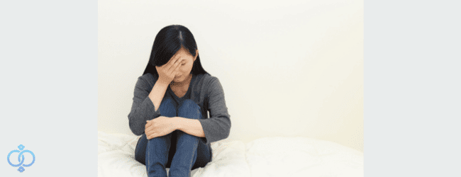 布団の上で膝を抱えて泣いている女性の写真