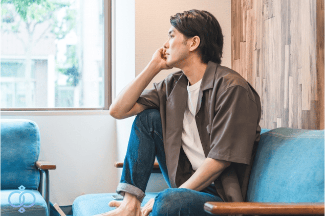 部屋で一人、窓の外を見ながら考え込んでいる男性の様子。精神的な不安や悩みを抱え、失踪につながる背景をイメージした場面。