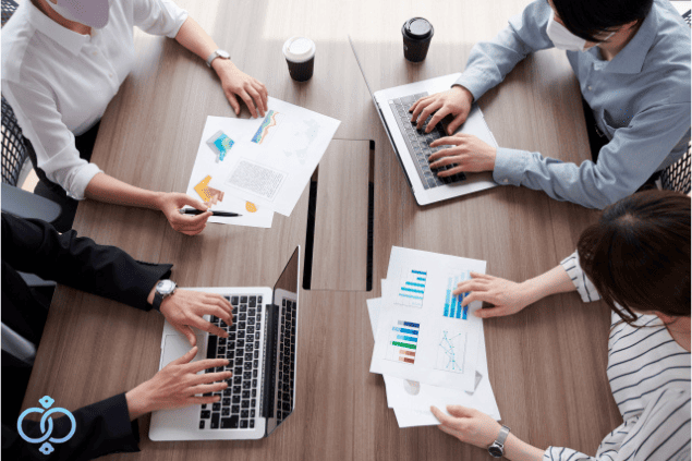 興信所に依頼できる企業調査の内容について、複数人で資料やパソコンを確認しながら調査項目を整理する様子。