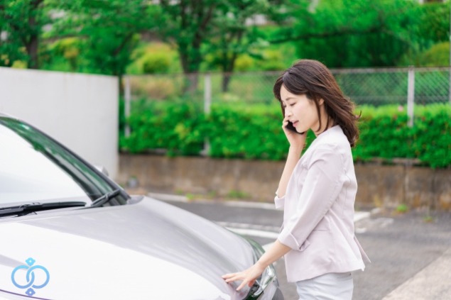 GPSを見つけた際の対処法として、車のそばで電話相談している女性のイメージ