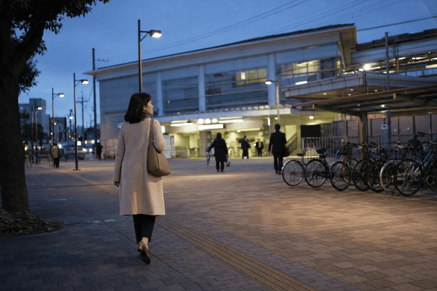夕方の駅前を一人で歩く女性の後ろ姿