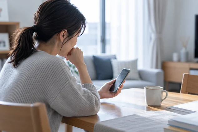 離れて暮らす高齢の親を心配し、自宅でスマートフォンを確認する女性